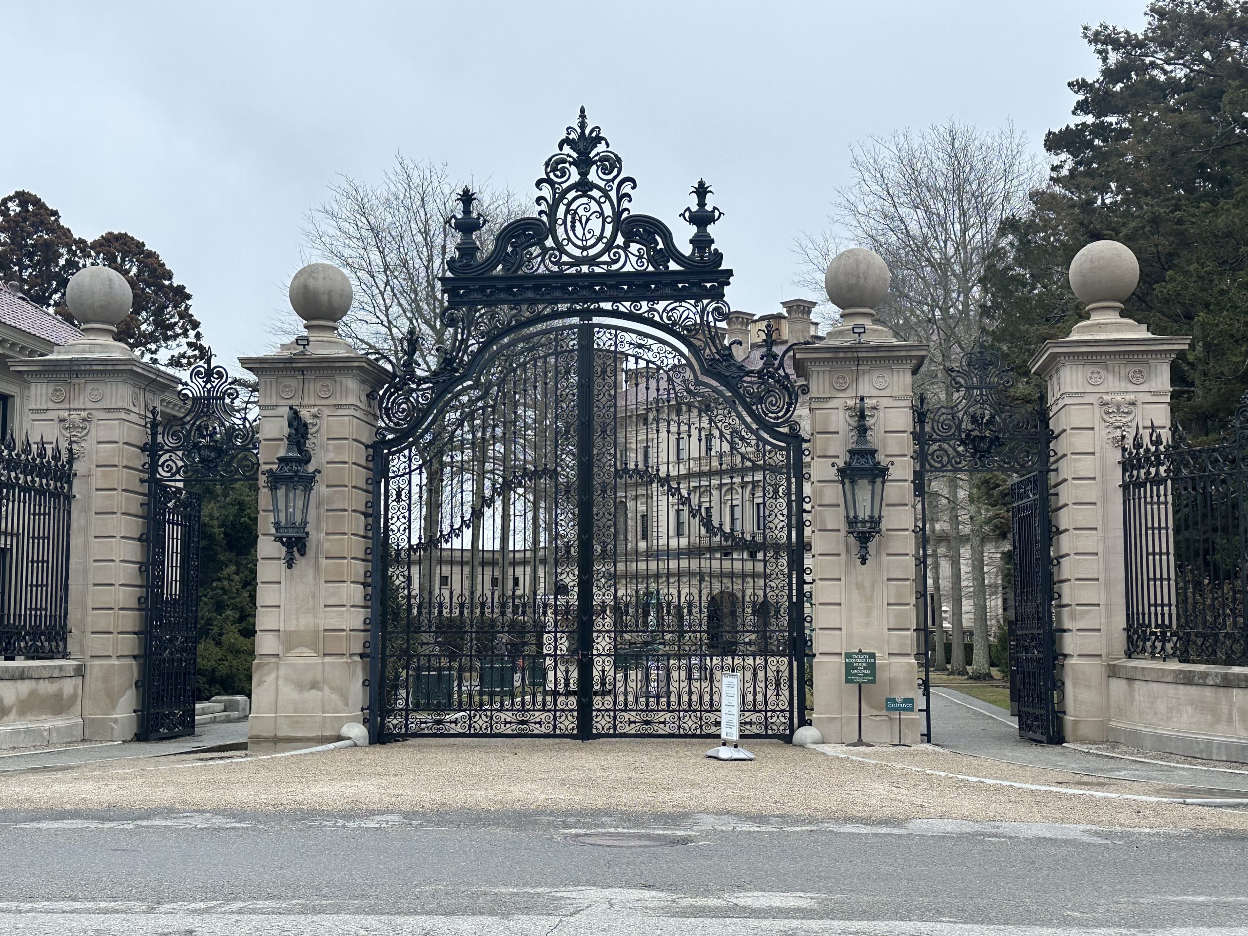 The Breakers entrance gate — ornate iron gates, limestone pillars, bare trees, gray sky