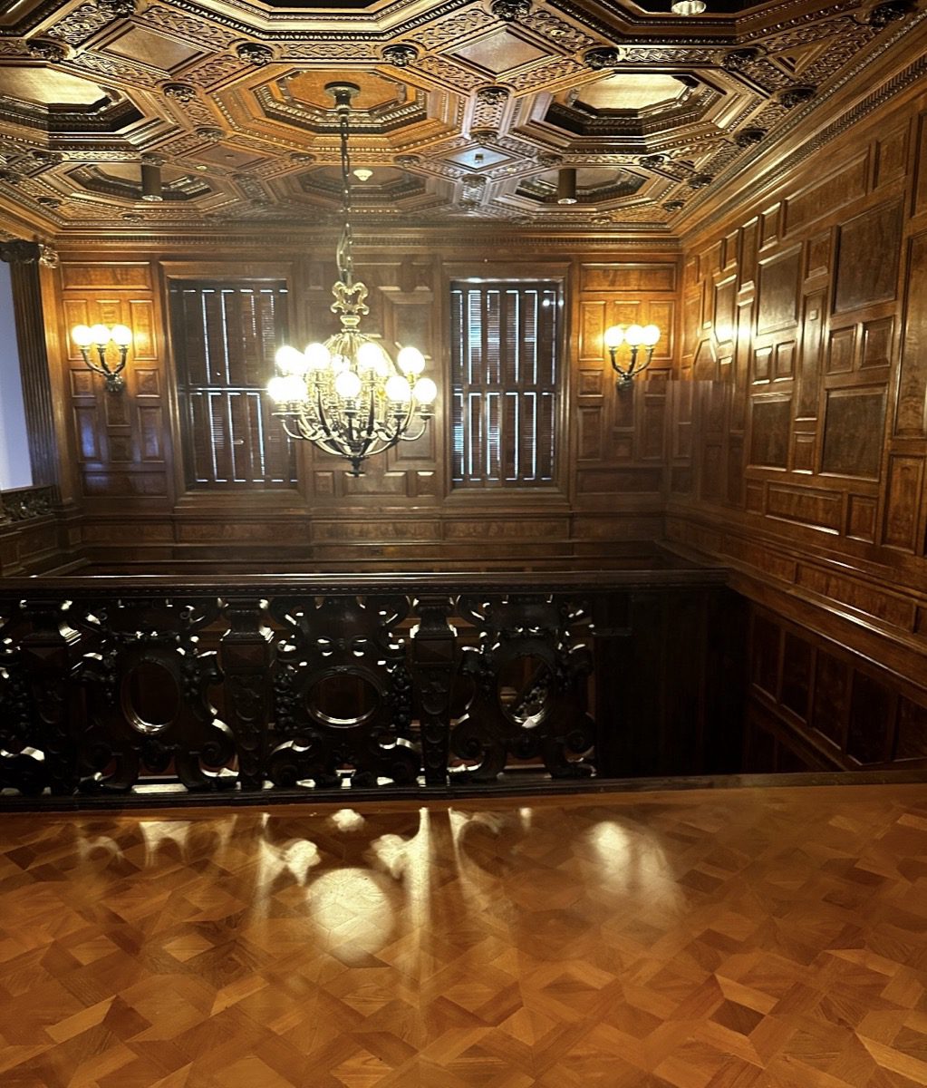 Carnegie Mansion interior — dark wood paneling, coffered ceiling, brass chandelier