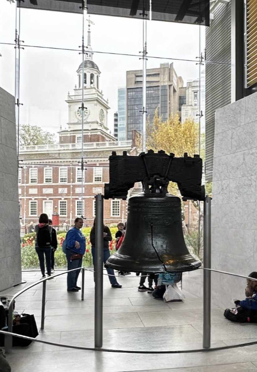 Liberty Bell inside Liberty Bell Center with Independence Hall visible through the glass behind