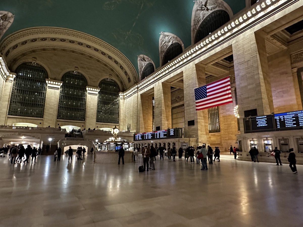 Grand Central Terminal main concourse — clock, American flag, turquoise ceiling, commuters